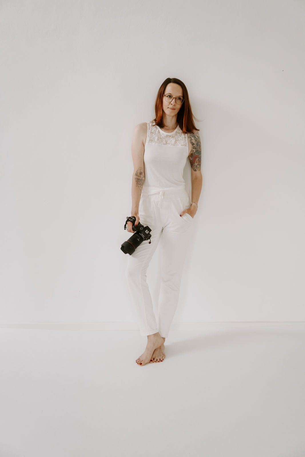 Portrait von Nadine in weißem Studio Setting mit ihrer Kamera in der Hand.
