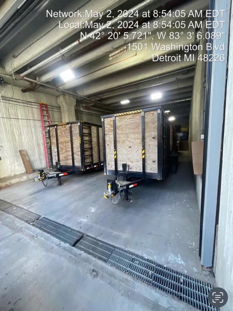 Two trailers in a loading dock; gray concrete, metal drain, overhead lights.