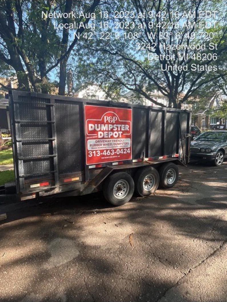 Dumpster trailer parked on a city street. Red and white Dumpster Depot sign. Silver car parked nearby.