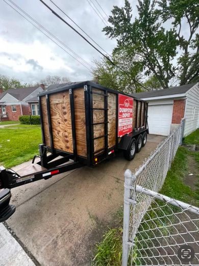 A black trailer with plywood sides parked on a driveway next to a house.