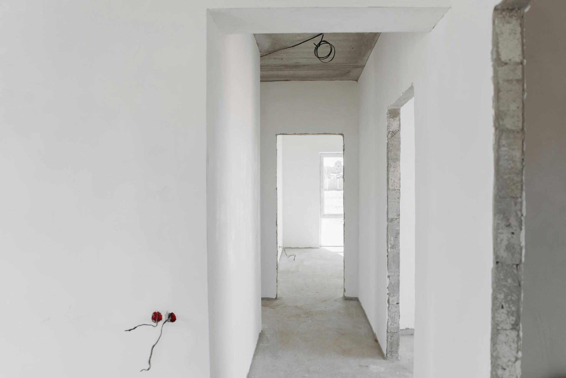 An empty hallway with white walls and concrete floors in a house under construction.
