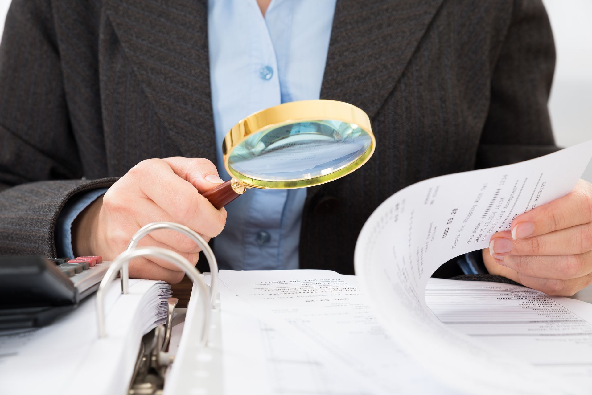 Close-up Of Businessperson Checking Bills With Magnifying Glass