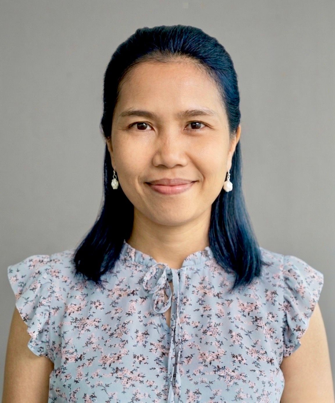 Woman with curly brown hair, wearing a white shirt and black blazer, smiling at the camera.