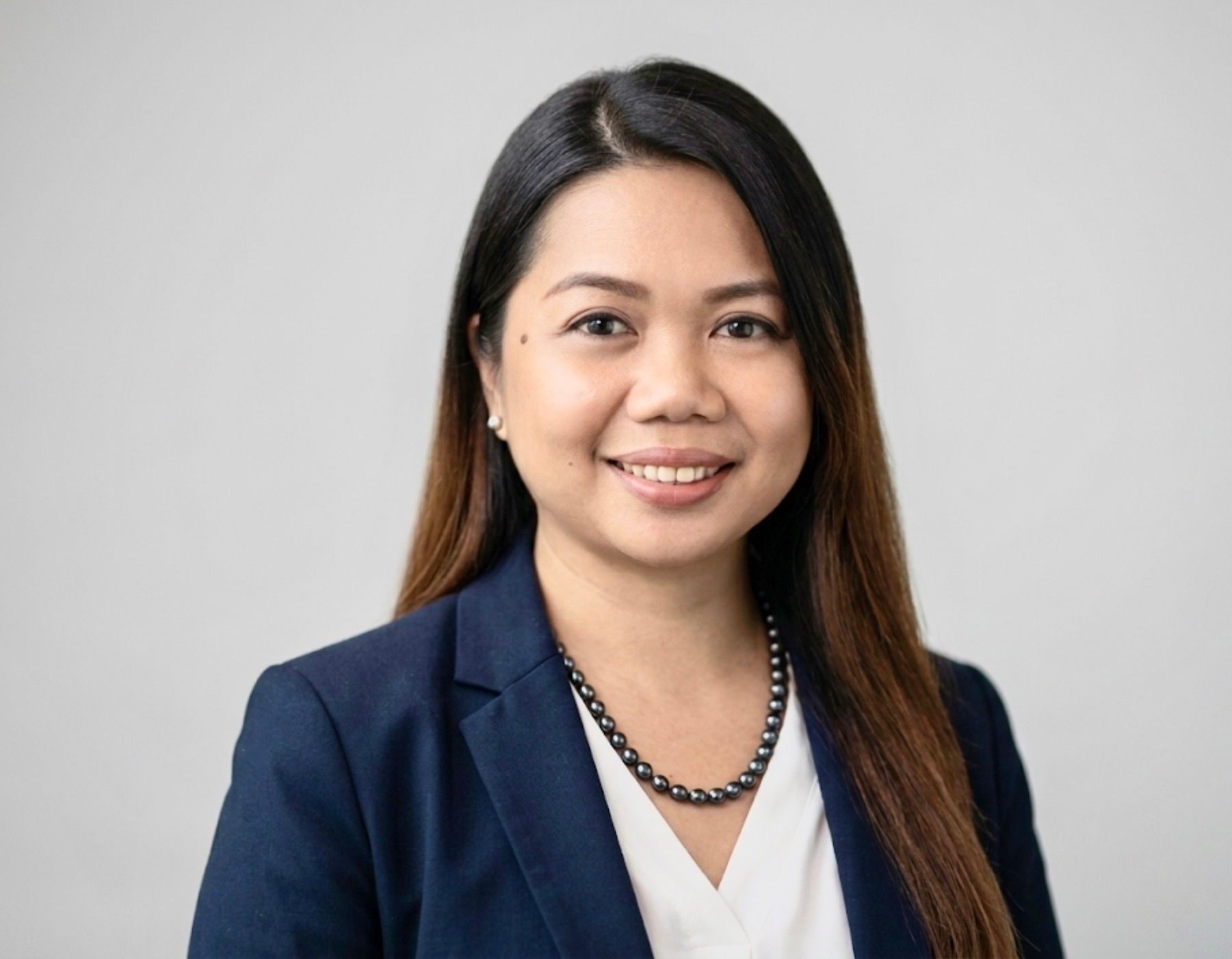 Woman with curly brown hair, wearing a white shirt and black blazer, smiling at the camera.