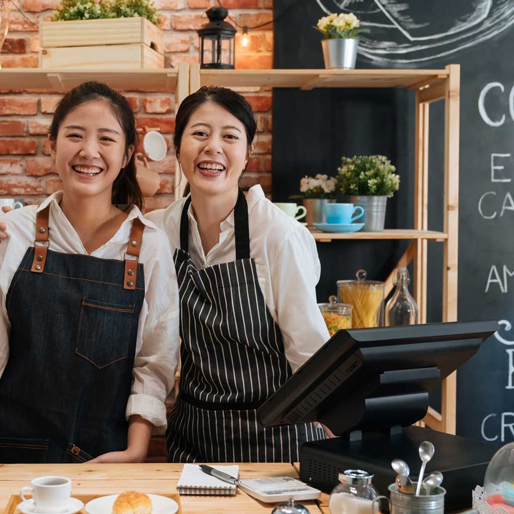 Two construction workers, smiling, leaning over a blueprint on a wooden counter.