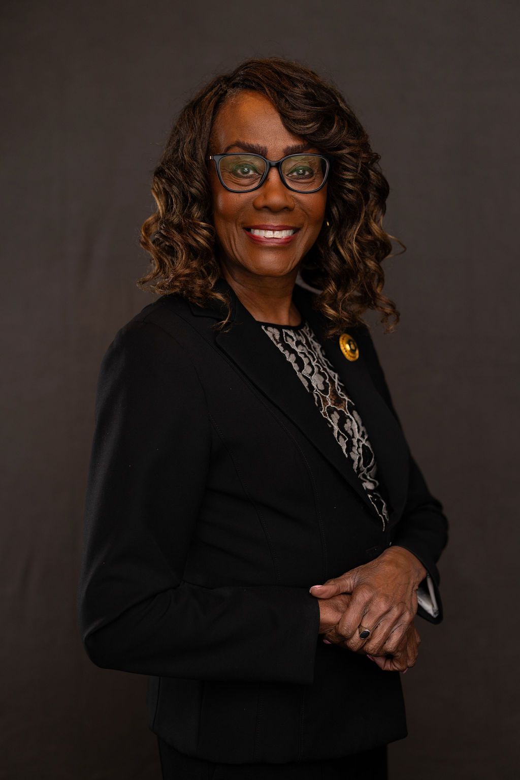 Woman with curly brown hair, wearing a white shirt and black blazer, smiling at the camera.