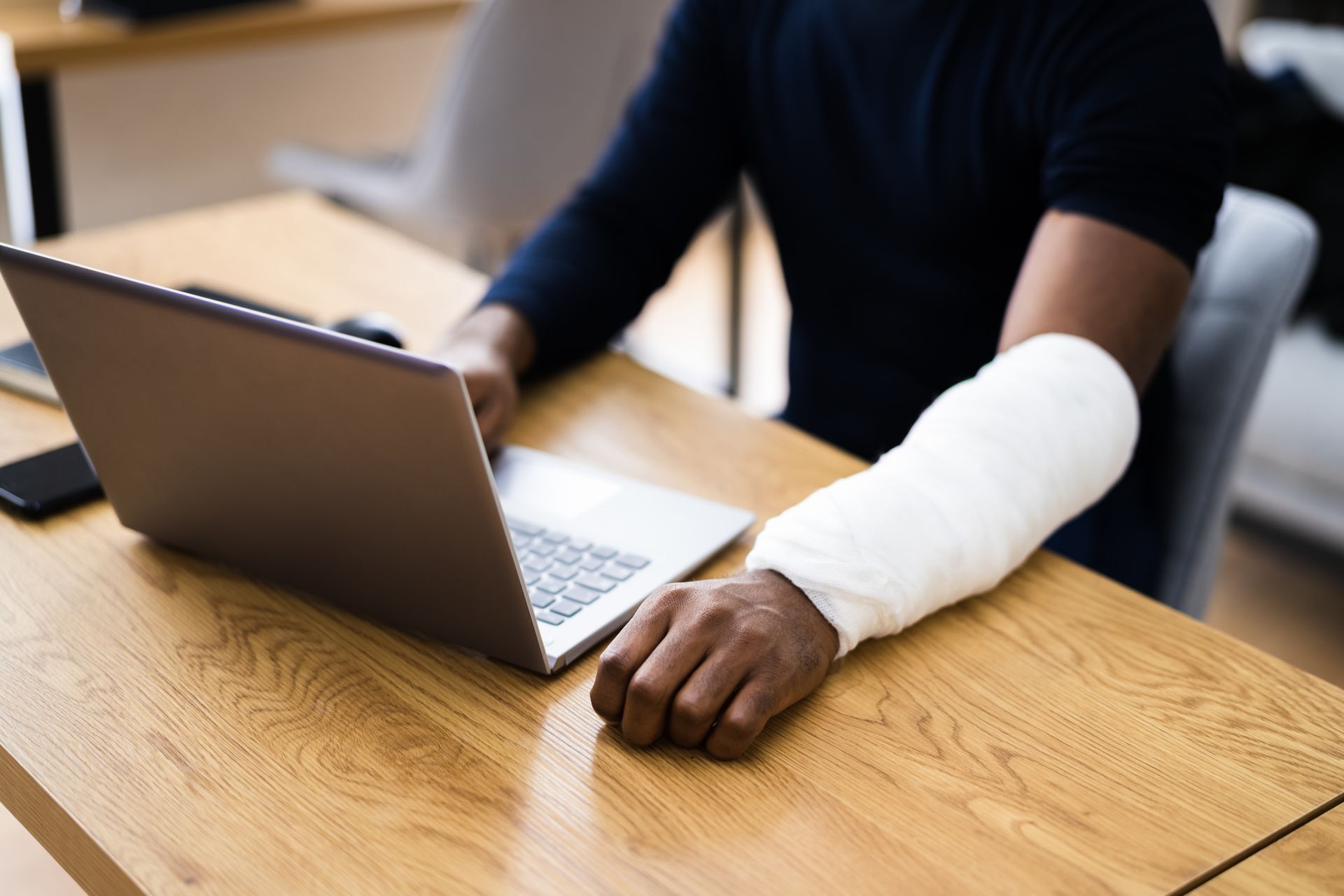 A man with a cast on his arm is using a laptop computer.