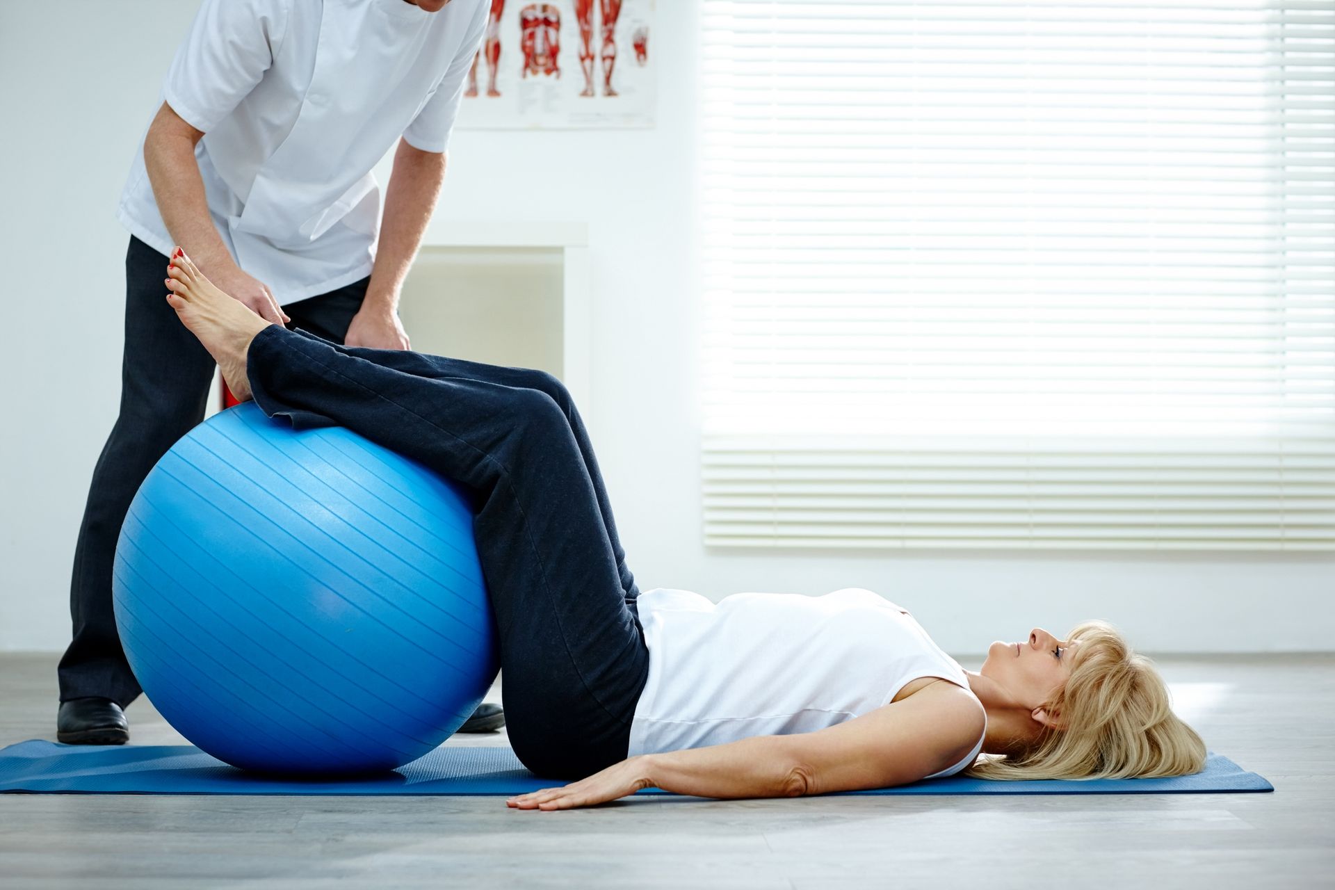 A woman is laying on a yoga mat with a blue exercise ball.