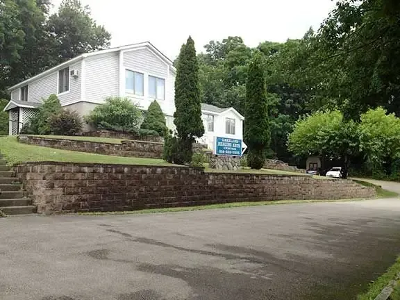 A large white house sits on a hill with trees in the background