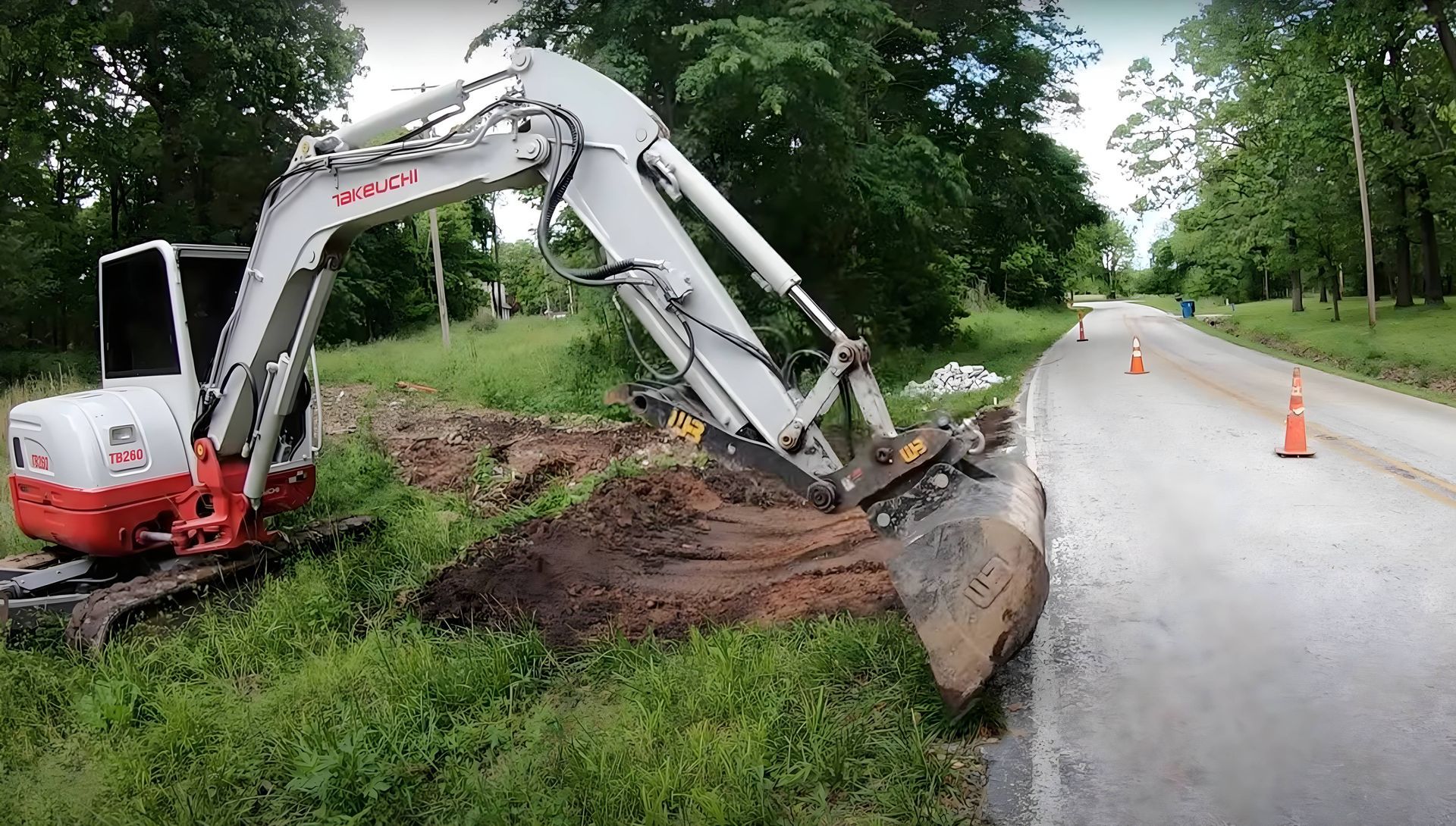 An red and white excavator cutting ditches for a culvert installation and improved drainage.
