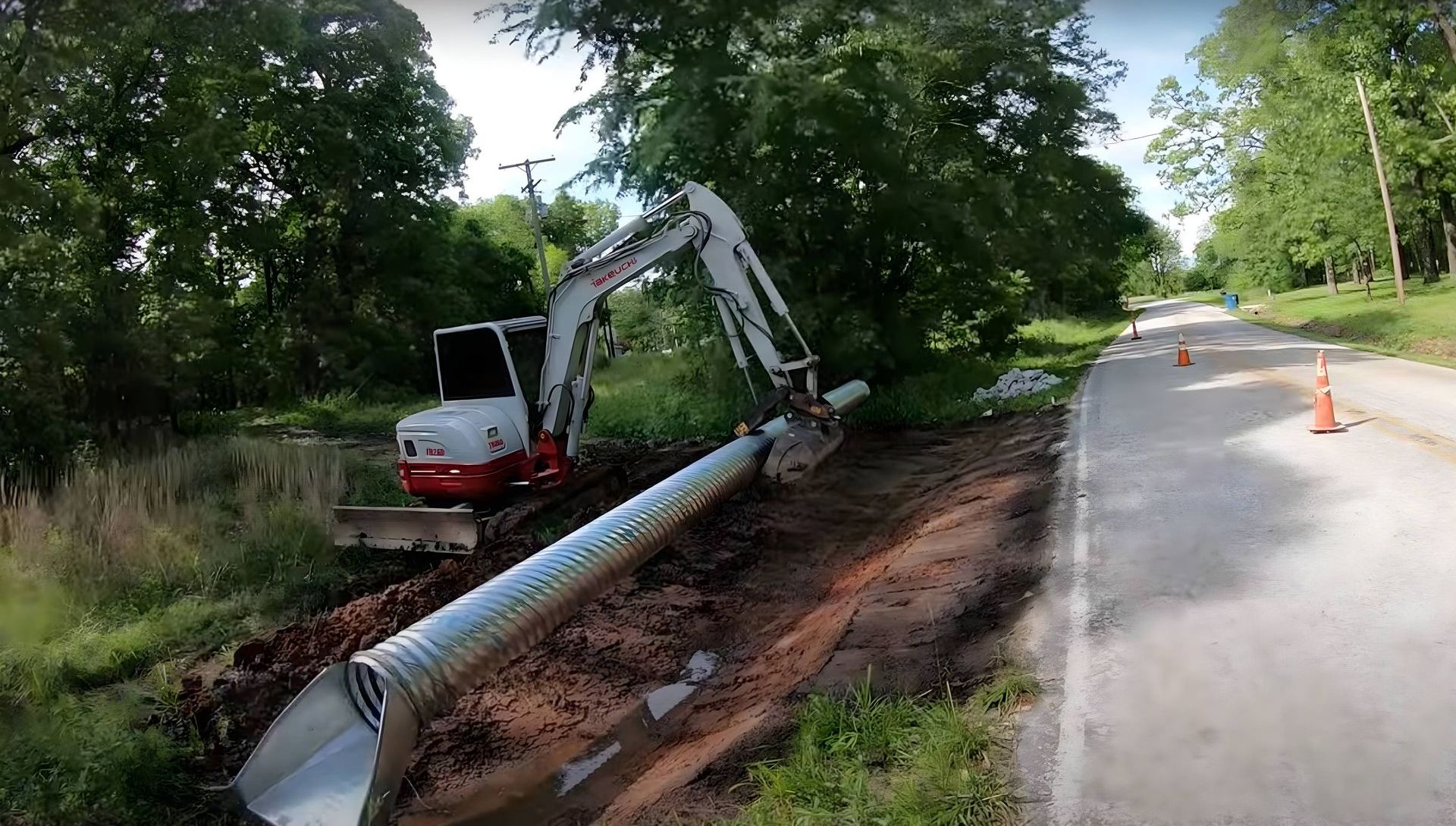 Mini excavator dropping a culvert pipe near a field access point.