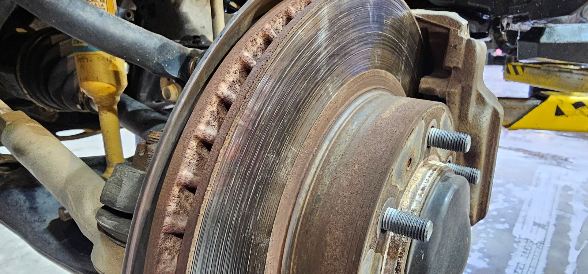 Close-up of a rusted car brake rotor and caliper with wheel studs in a workshop | Masters Auto Group