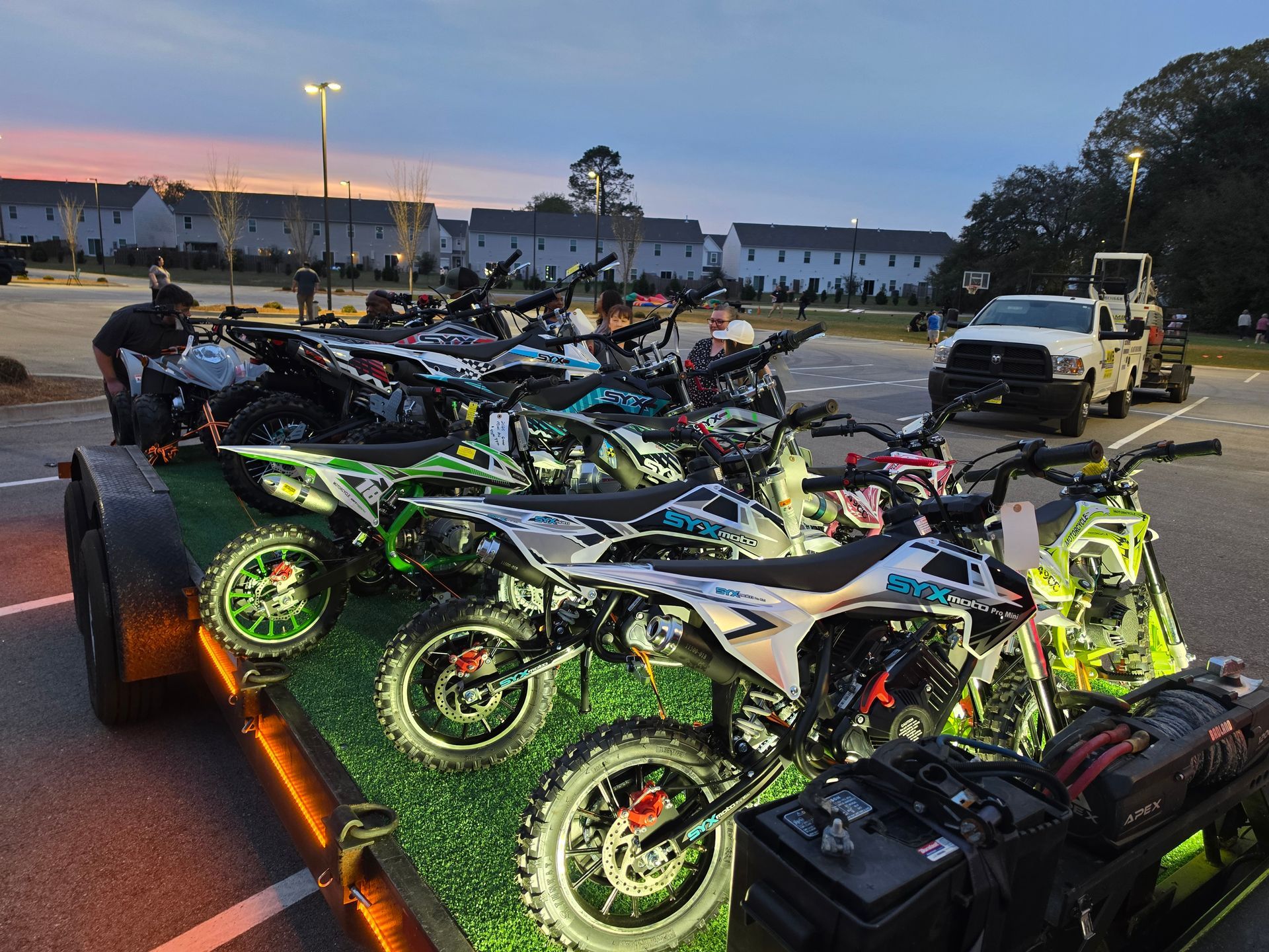 Row of neon-lit dirt bikes on a trailer at dusk in a parking lot | Masters Auto Group