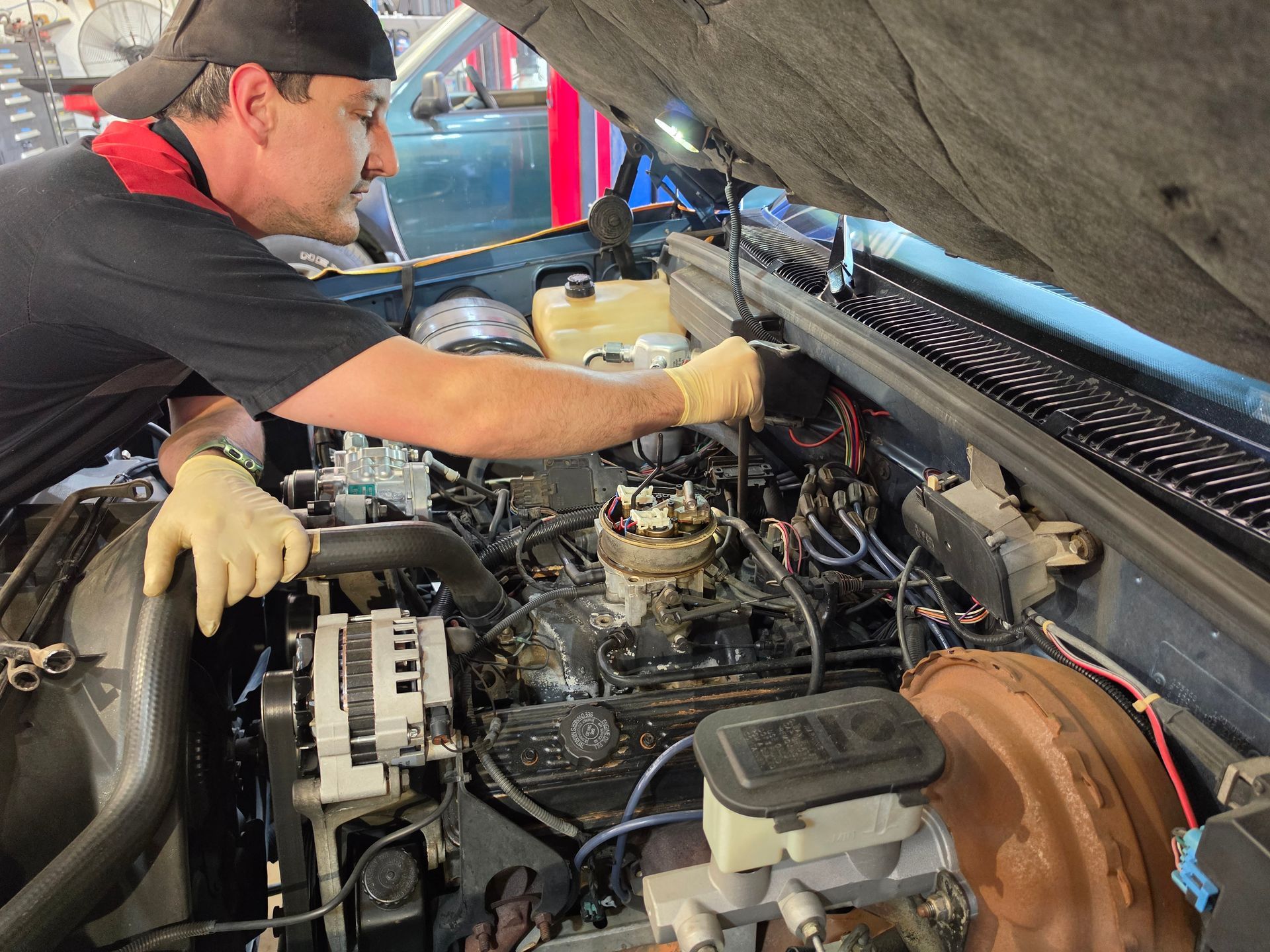 Mechanic working under a car hood, inspecting the engine bay with tools and gloves. | Masters Auto Group