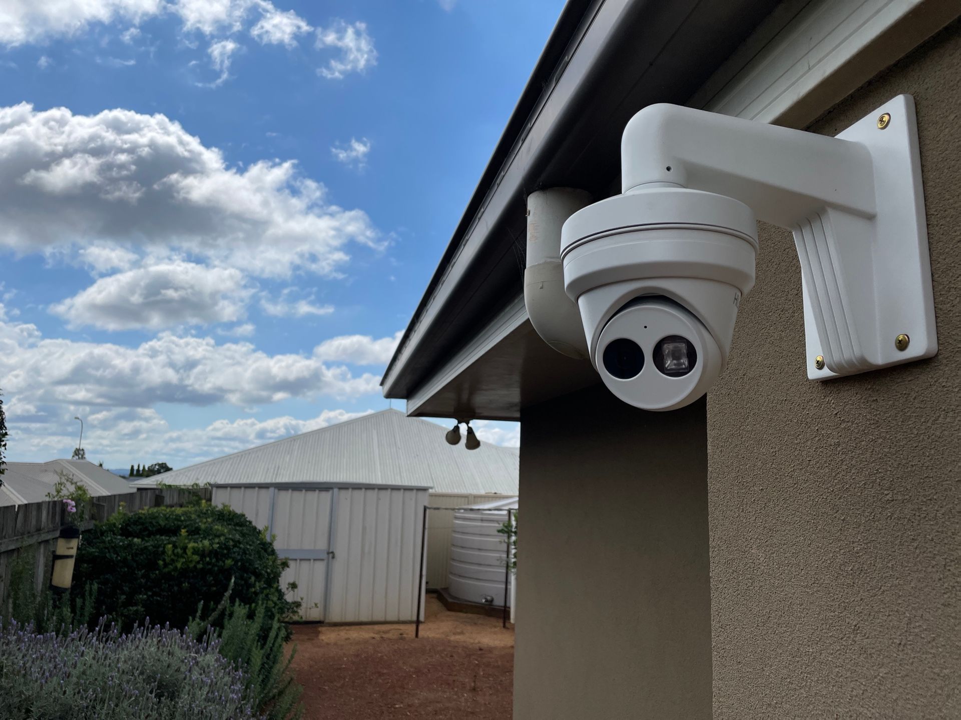 White Security Camera Mounted on Beige Exterior Wall Under a Roof, Blue Sky, Backyard — Frontier Security in Dalby, QLD