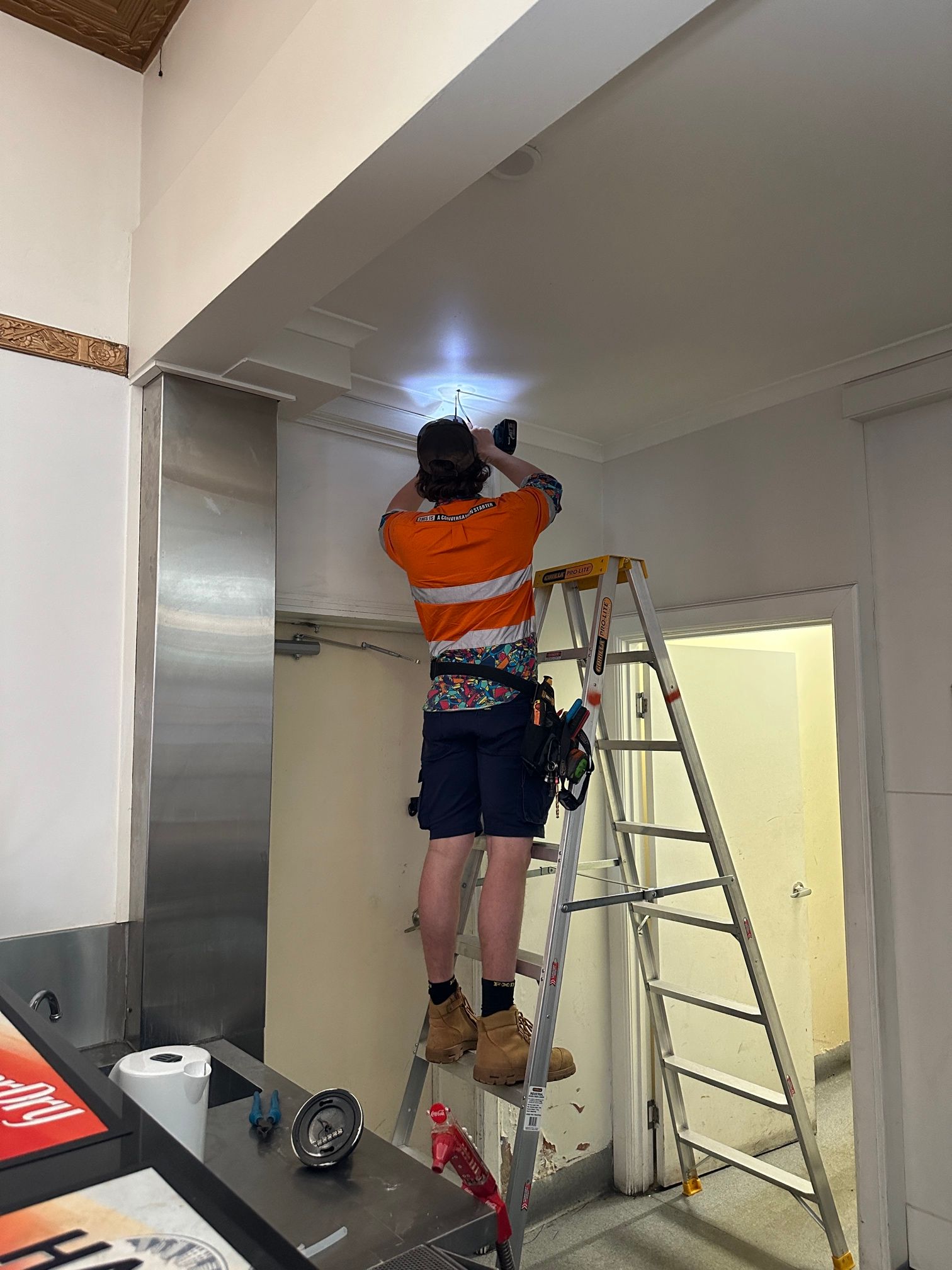 Man in Work Clothes on a Ladder, Installing Something on the Ceiling. Indoor Setting — Frontier Security in Gatton, QLD