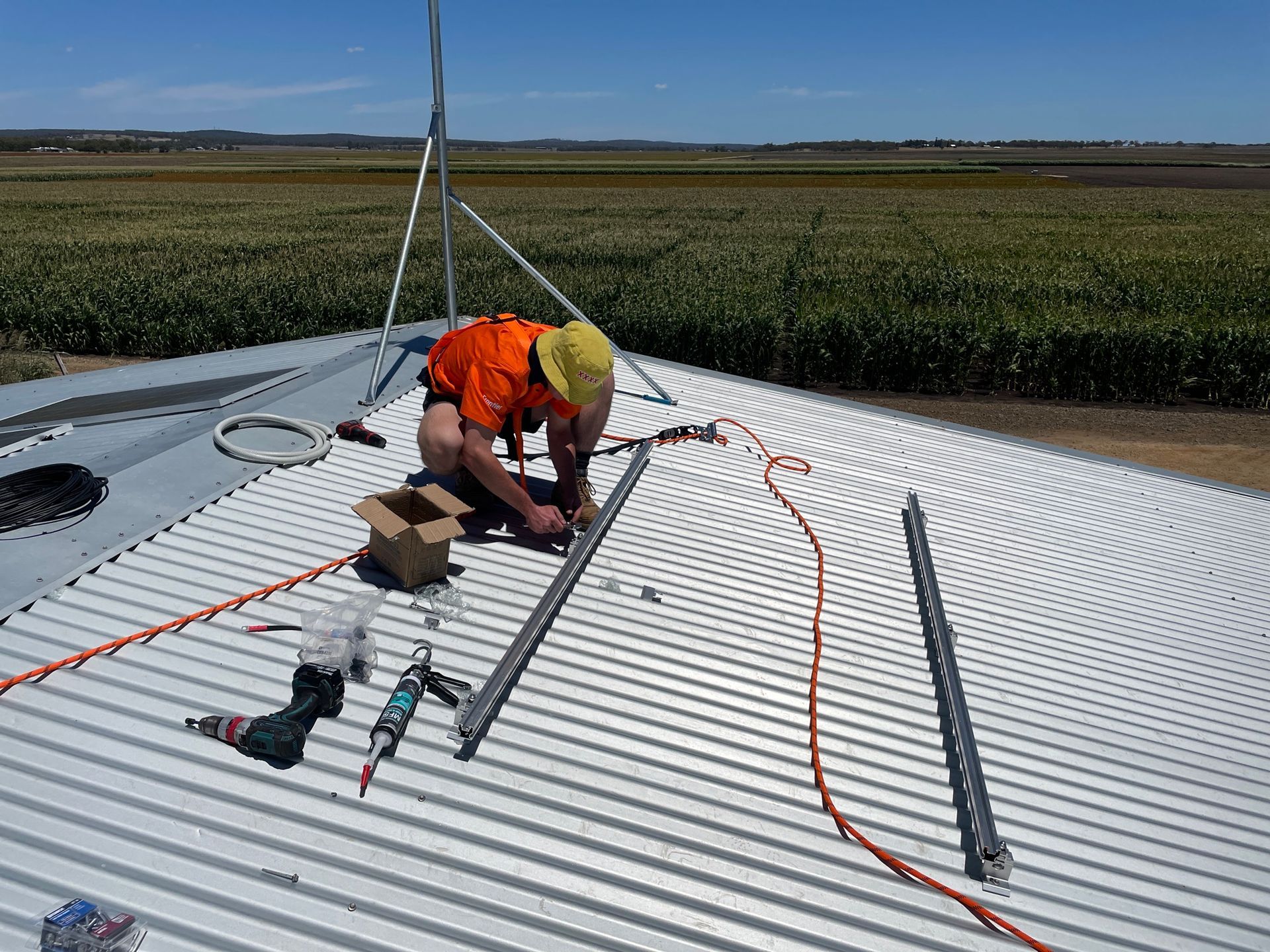 Man on a Metal Roof Installing Solar Panel Rails, Wearing Safety Gear — Frontier Security in Chinchilla, QLD