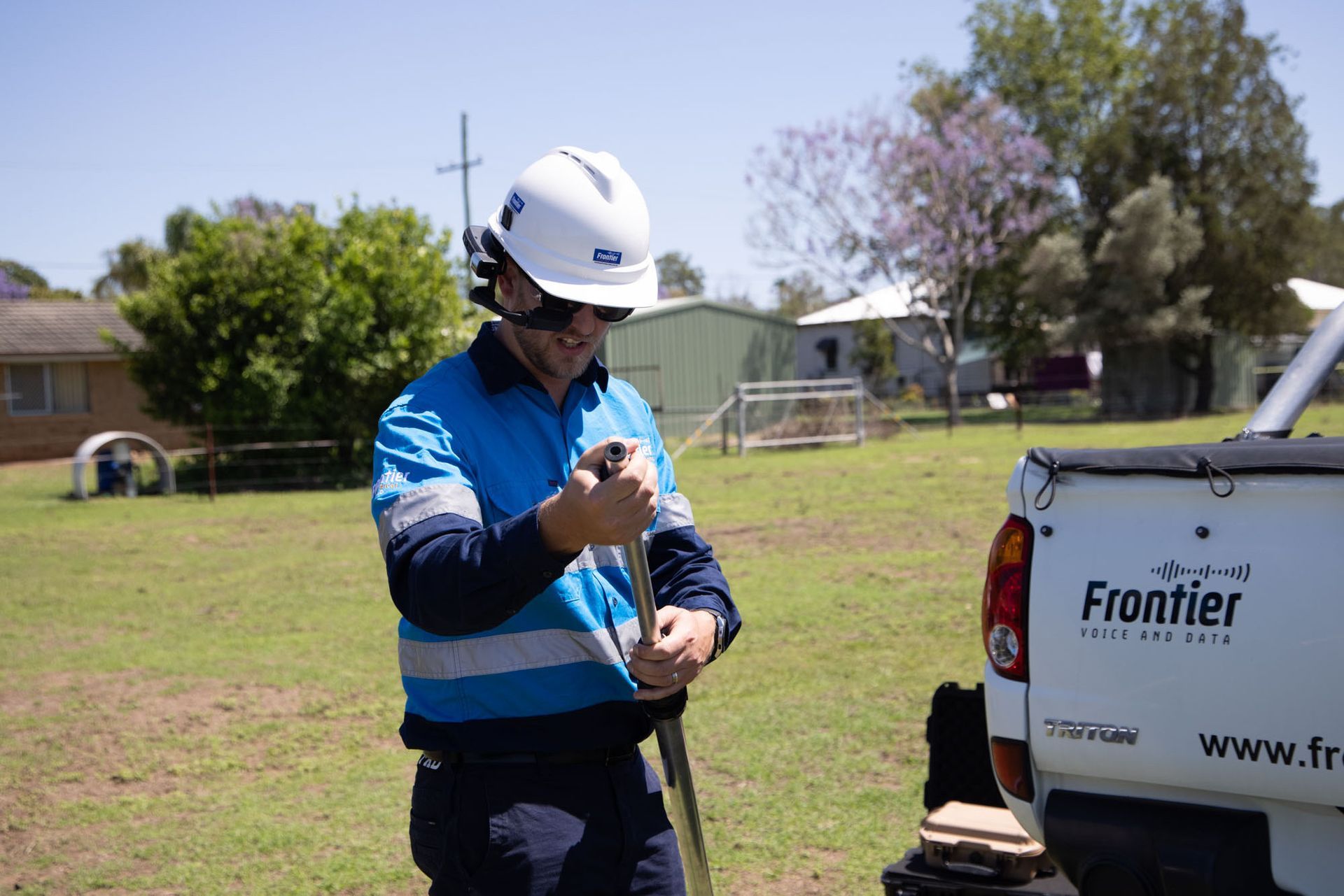 Man in Work Clothes and Helmet, Next to a Frontier Truck, Inspecting a Tool in Grassy Area — Frontier Security in Dalby, QLD 
