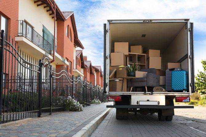 Moving truck loaded with boxes on a residential street beside apartment buildings.