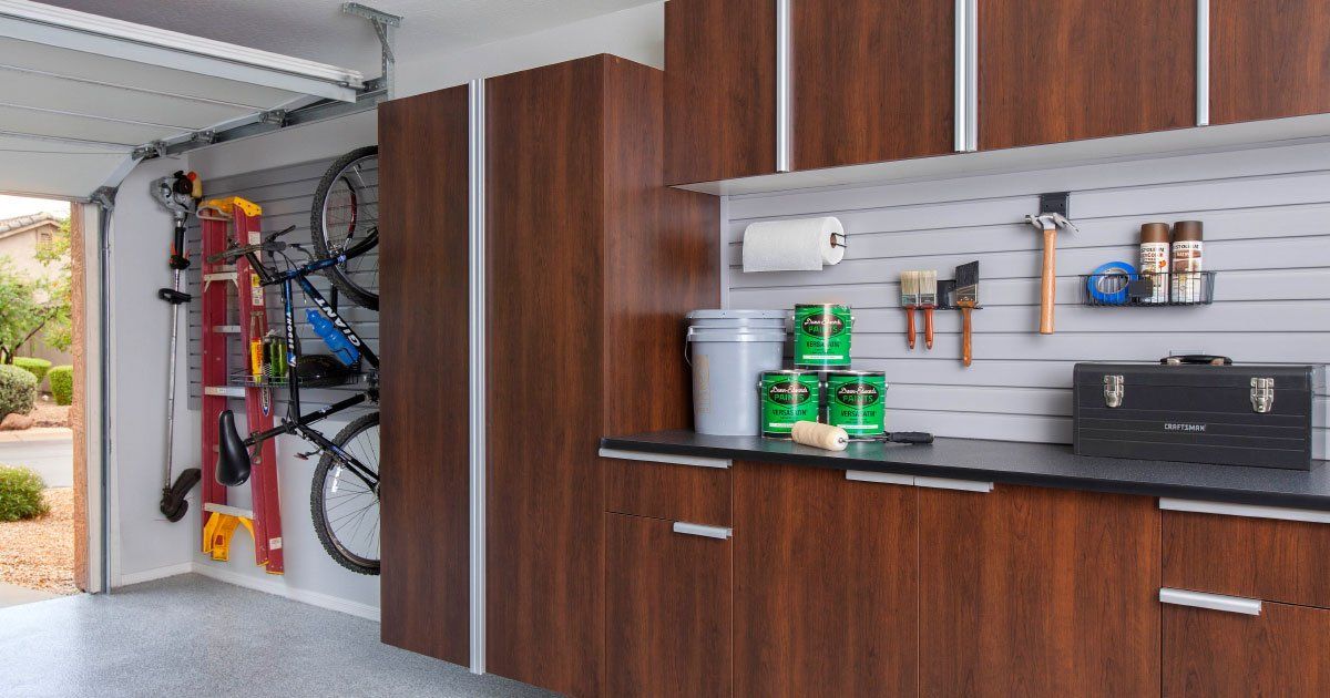 a garage with wooden cabinets , a bicycle rack , a ladder , and a workbench .