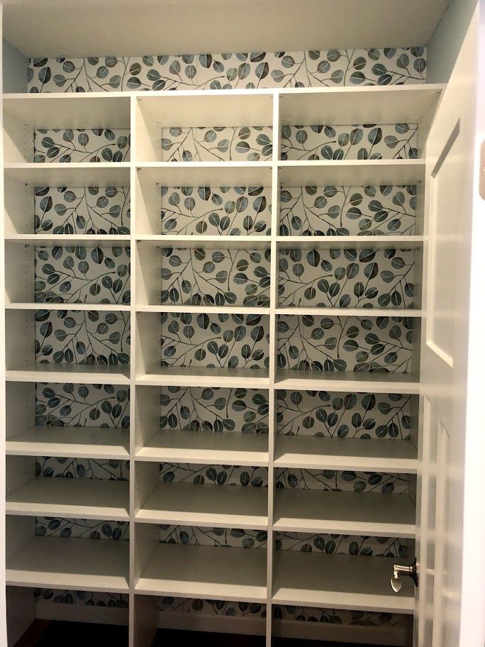 a walk in closet with shelves and wallpaper on the wall .