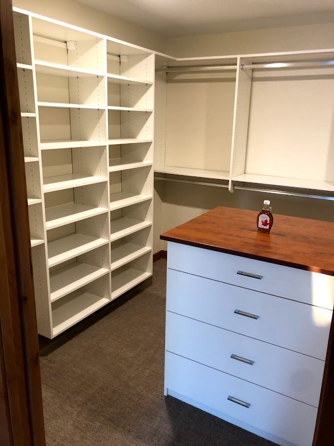 a walk in closet with lots of shelves and a dresser with a bottle of syrup on it .