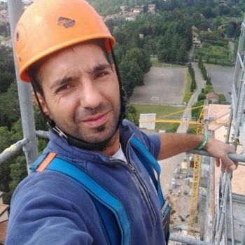 Un uomo che indossa un casco arancione si scatta un selfie su un'impalcatura.