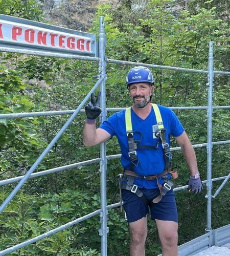 Un uomo che indossa una camicia blu e un casco è in piedi davanti a un'impalcatura.
