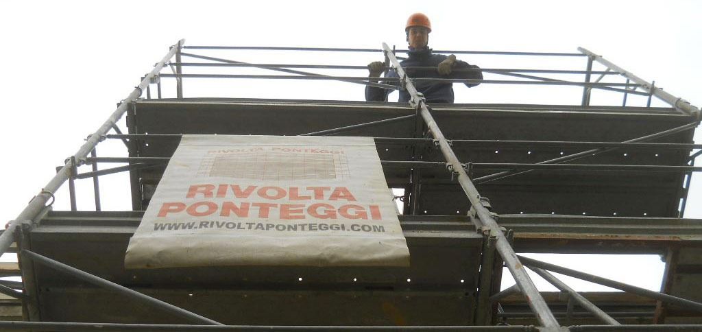 Un uomo in piedi in cima a un'impalcatura con un cartello che dice rivolta pontaggi