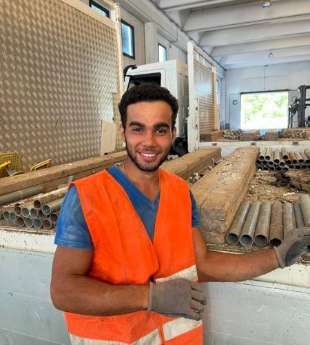 Un uomo con un gilet arancione è in piedi davanti a una pila di tubi.