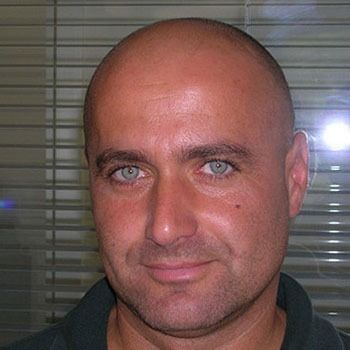 Un uomo con gli occhi verdi sorride alla telecamera del personale