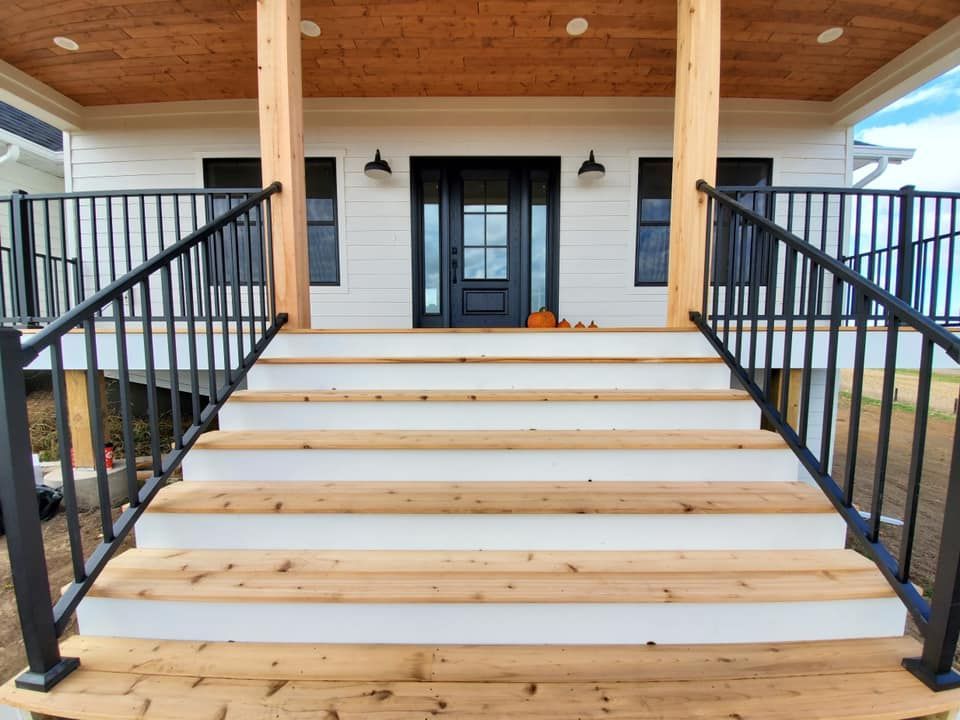 The front porch of a house with wooden steps and a black railing.