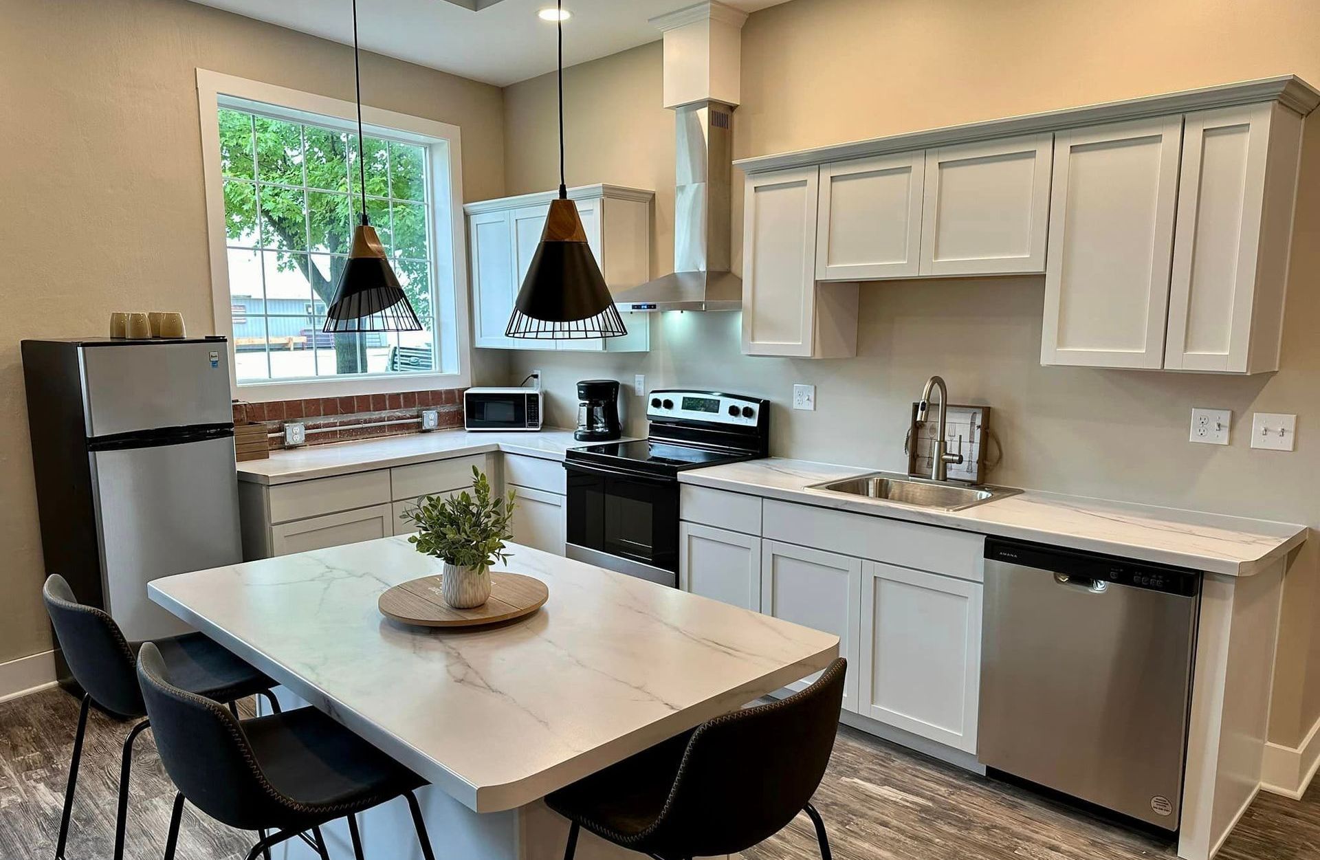 Modern kitchen with white cabinets, stainless steel appliances, and a marble-top island with chairs.