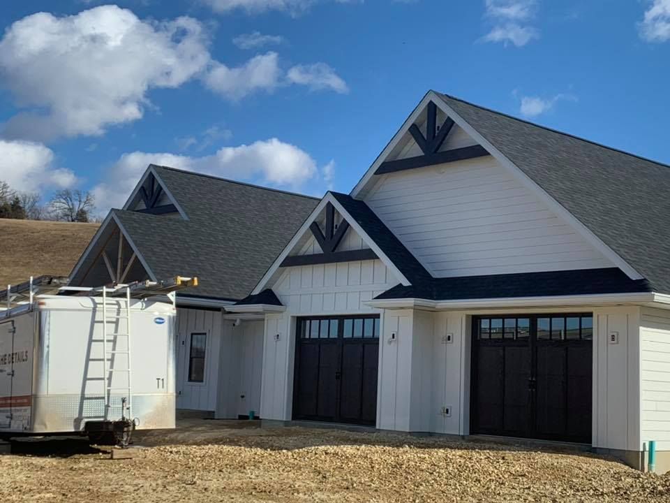 A white house with a black garage door is being built behind Cummings trailer