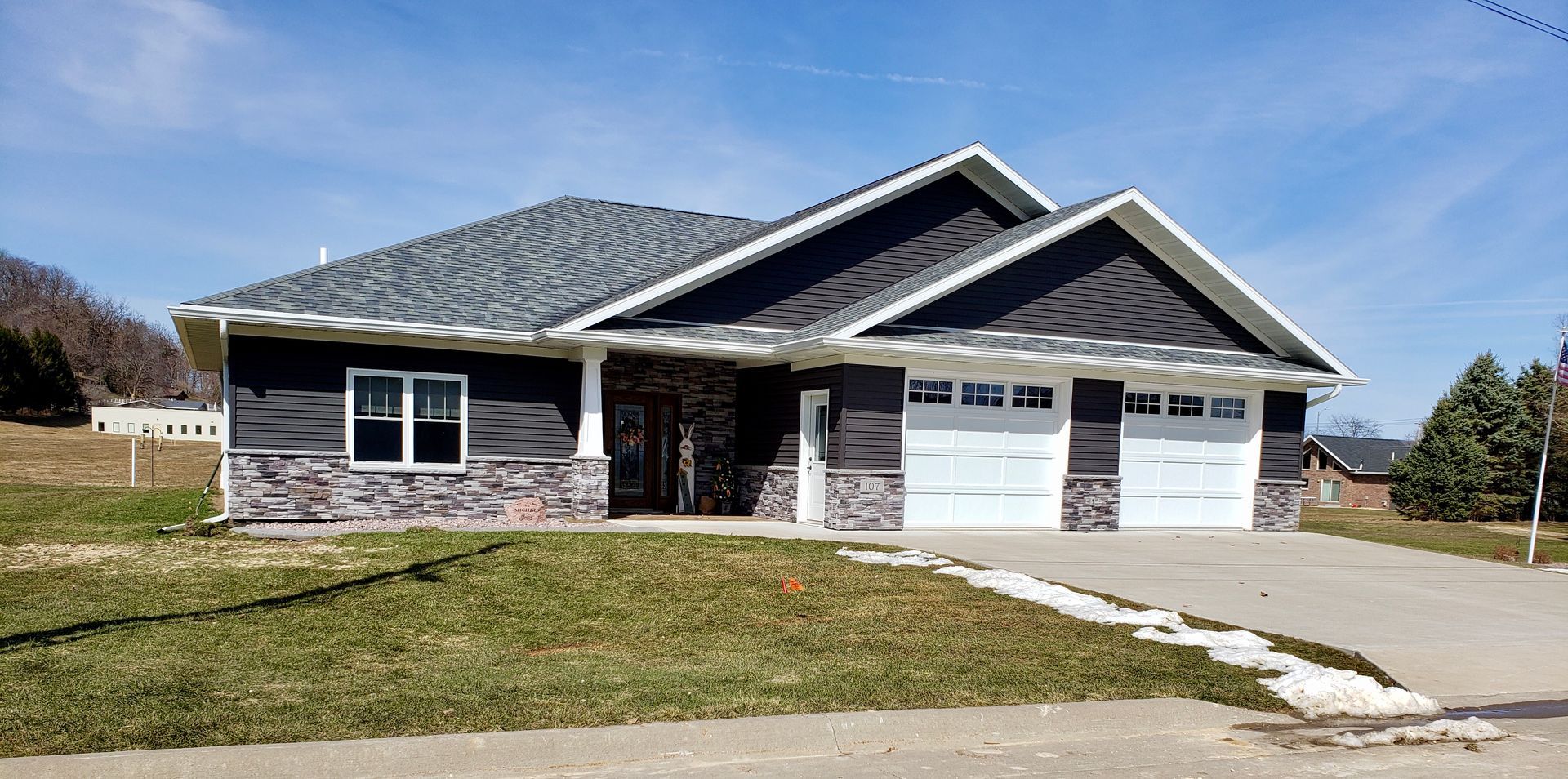A large house with a gray roof and white garage doors is sitting on top of a lush green field.