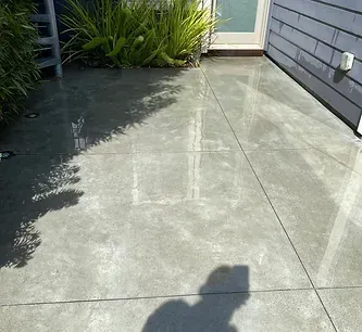 A shadow of a person is cast on a concrete floor in front of a house.