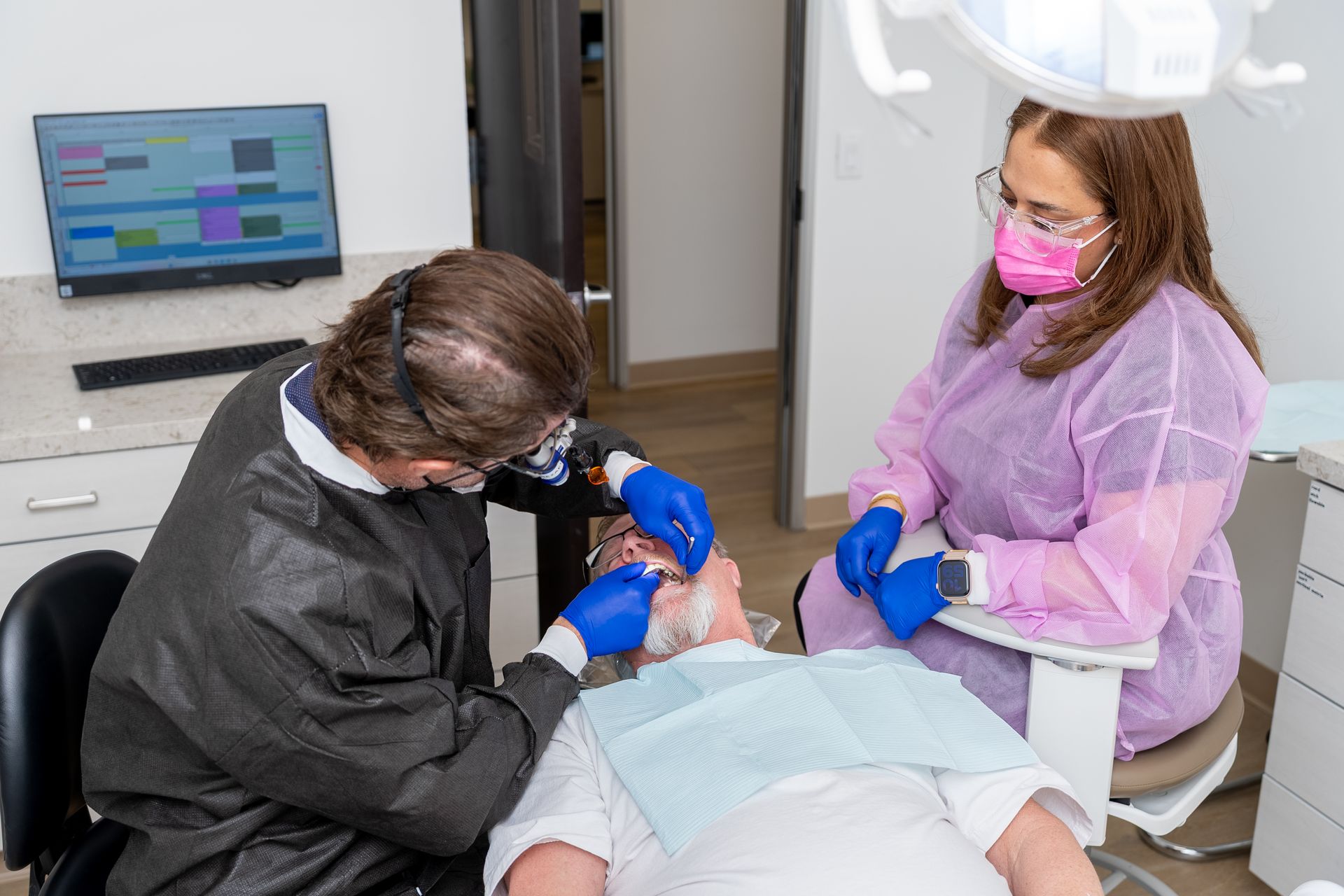 Dentist and assistant working on patient's teeth in a dental office. Both wear masks and gloves.