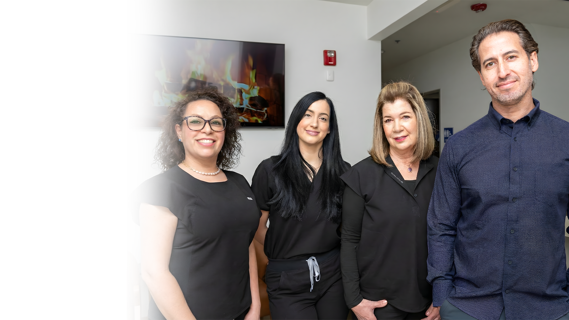 Four people standing in an office: a woman with glasses, another in scrubs, another with blonde hair, and a man, smiling.