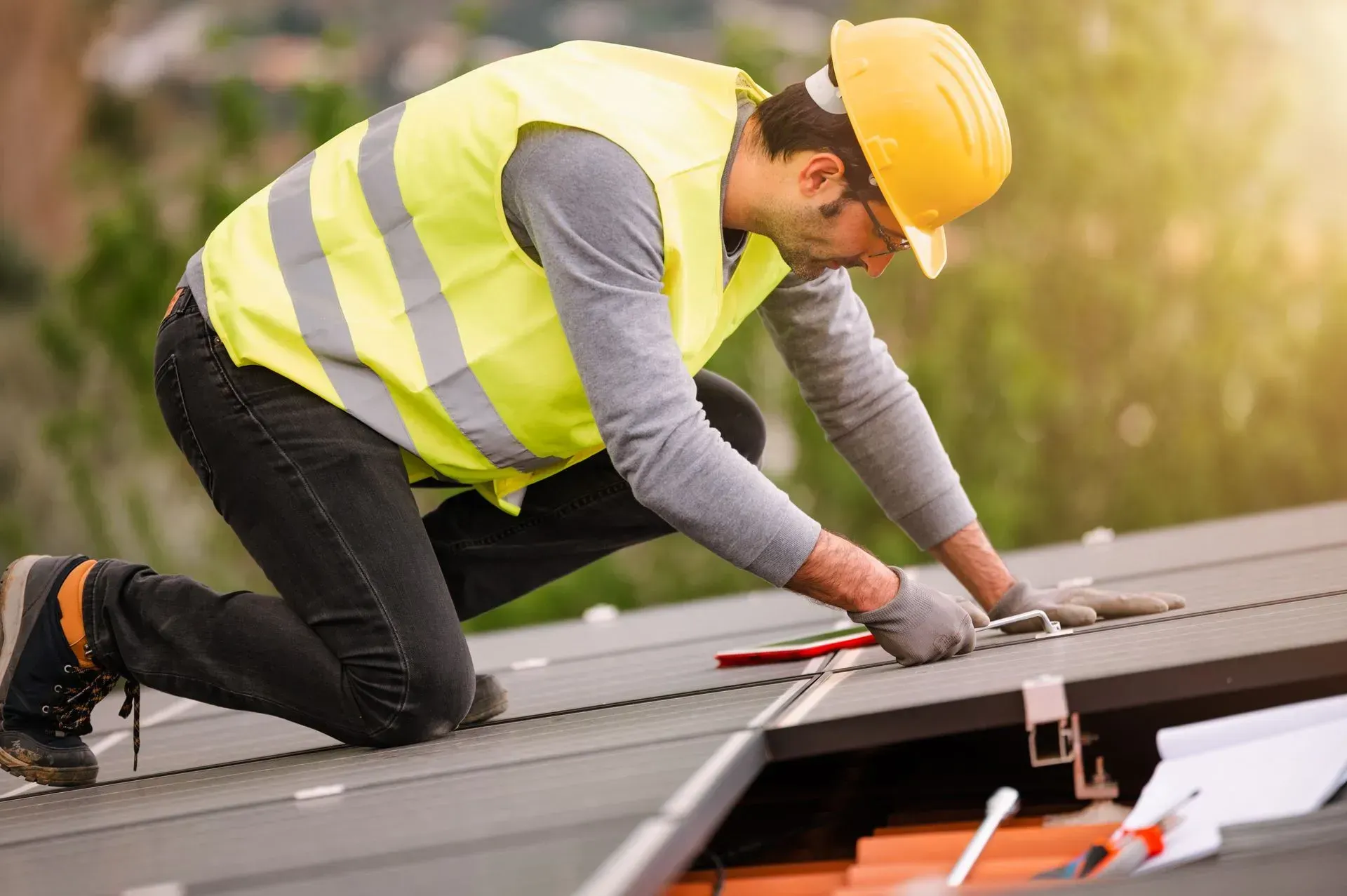 Solar panel installer working on a rooftop, wearing a yellow hardhat and safety vest.