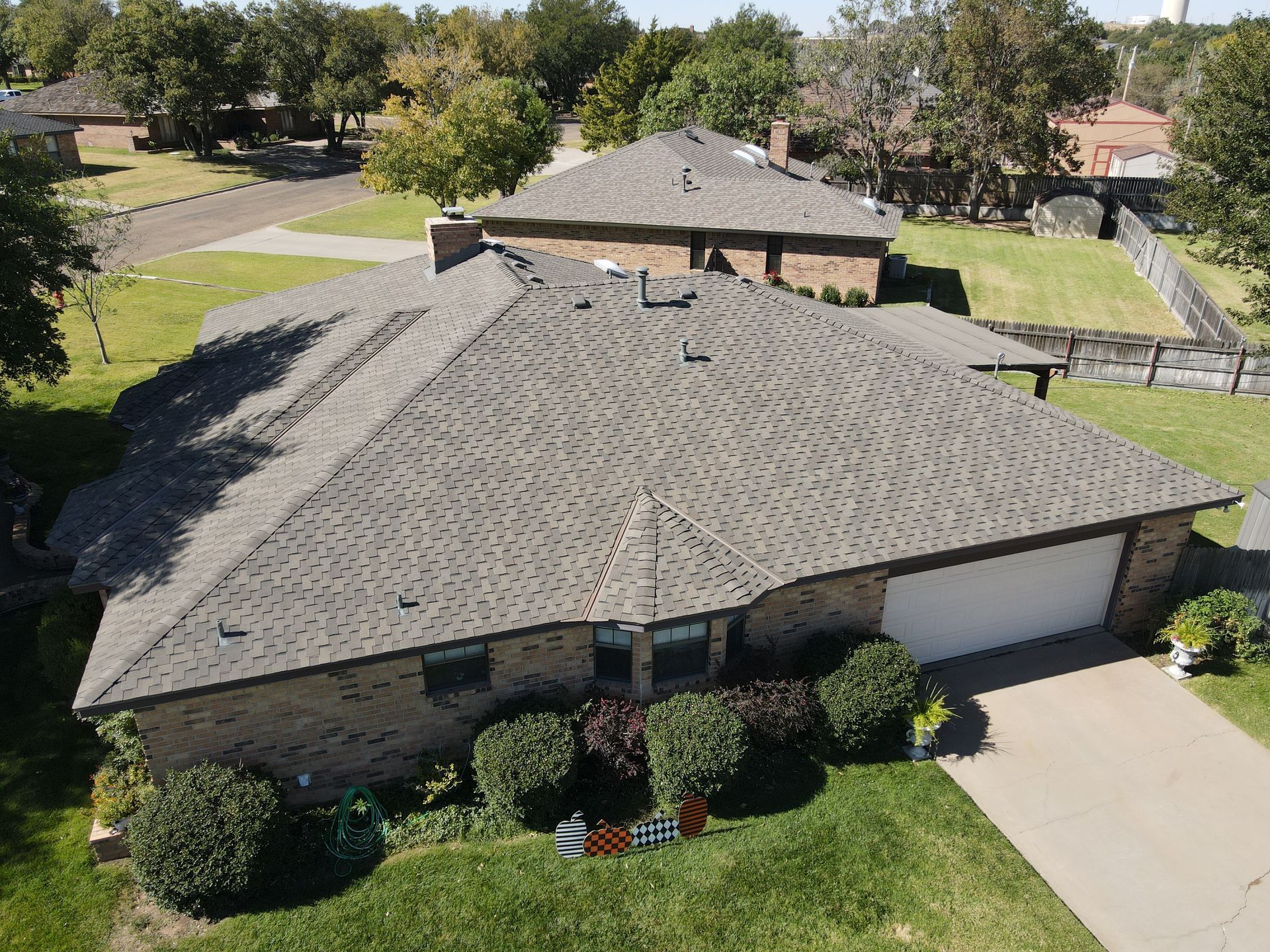 Overhead view of a house with a gray roof, brick exterior, and attached garage. Green lawn with bushes.