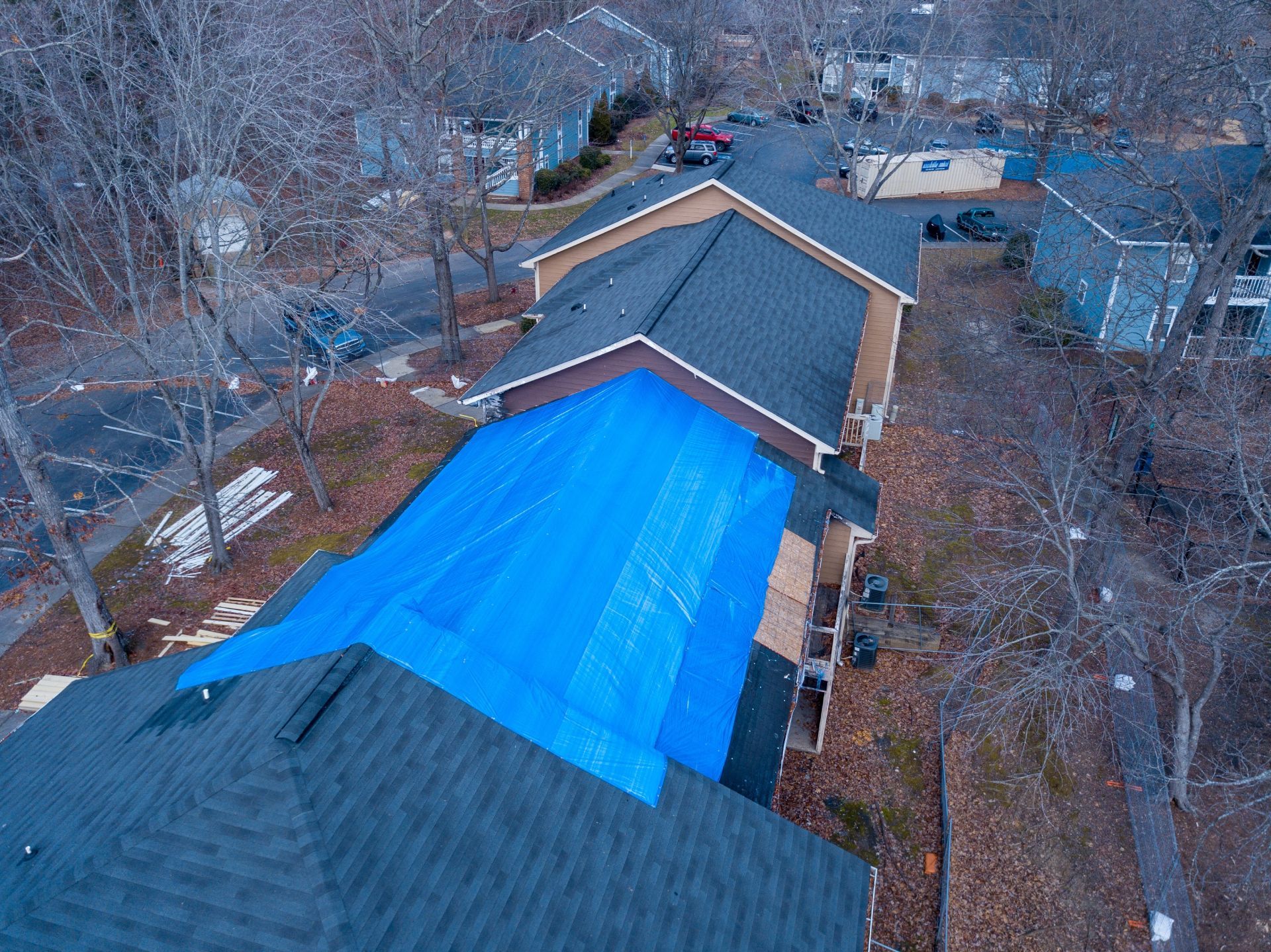 Overhead view of a building with a blue tarp covering part of a dark shingled roof.
