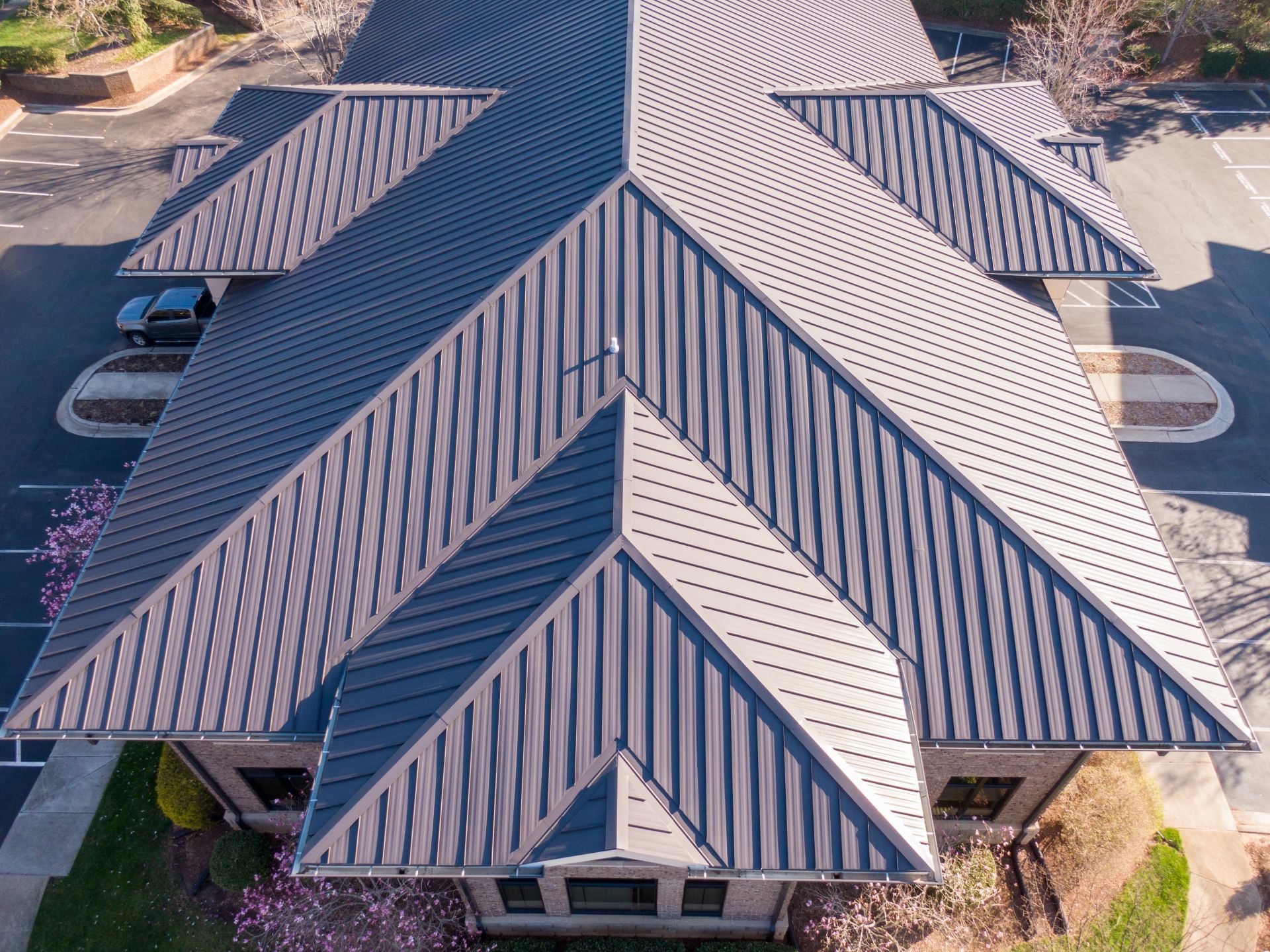 Aerial view of a building with a dark gray metal roof. Parking lot and landscaping visible.