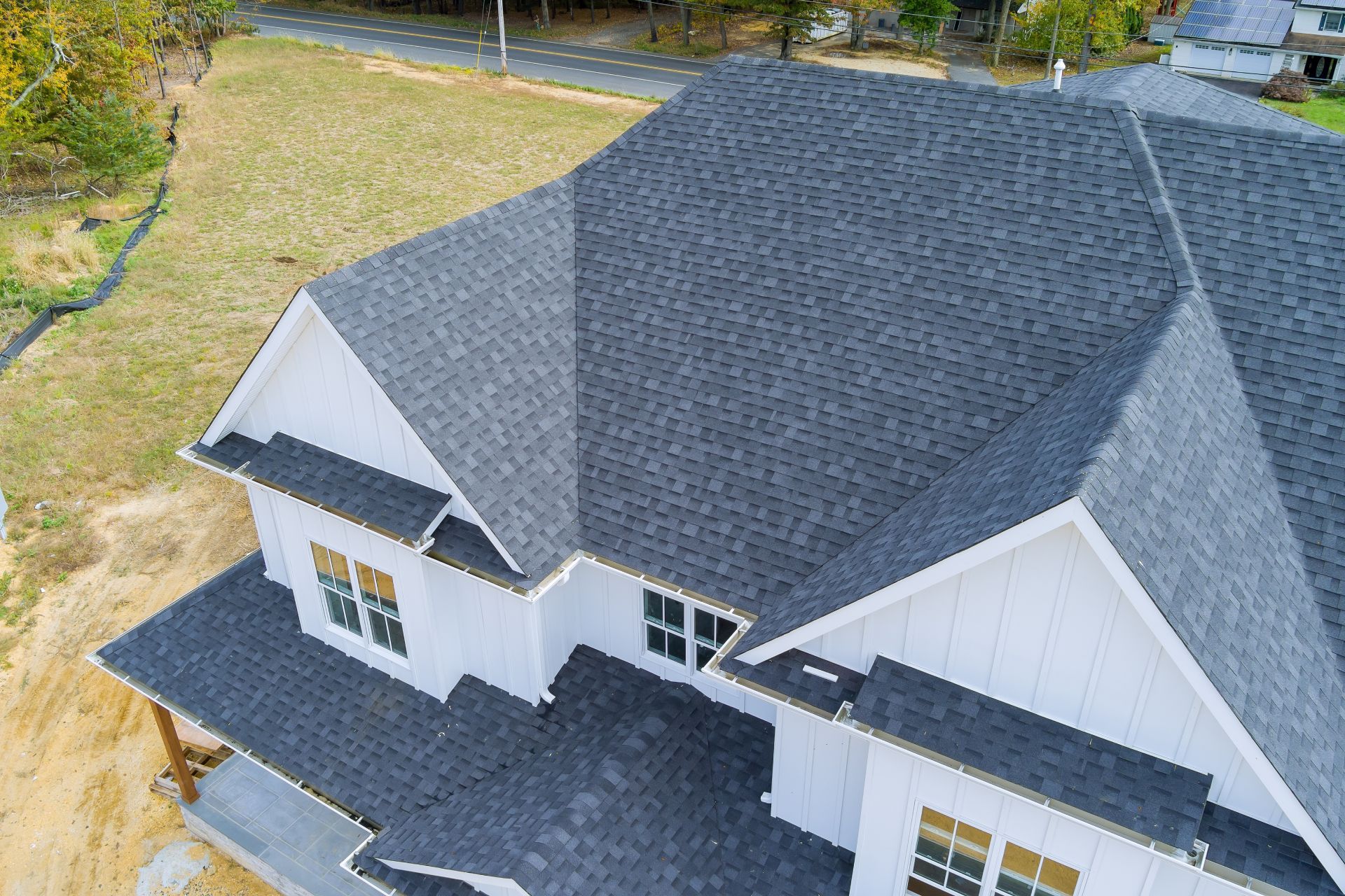 Overhead view of a house with a dark gray shingled roof and white siding, surrounded by grass and trees.