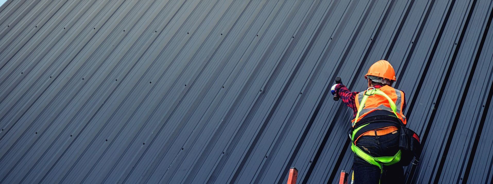 Roofer in safety gear on a sloped, corrugated metal roof.