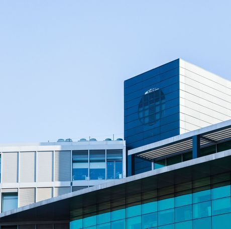 Modern building with blue glass facade and boxy white and blue sections against a clear blue sky.