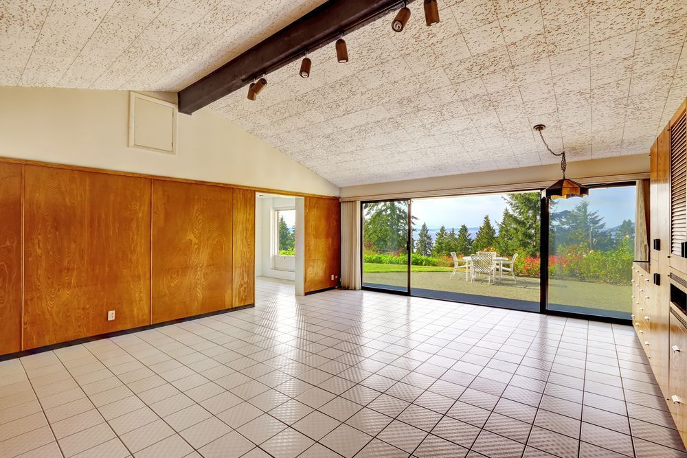Spacious room with white tile floor, wood paneling, and a large sliding glass door opening to a green outdoor view.