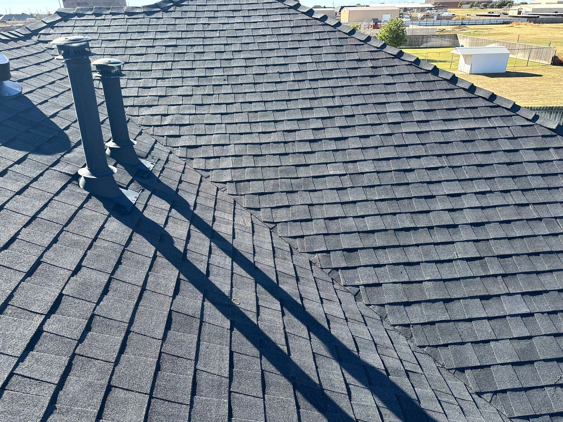 Black asphalt shingle roof with two tall vents casting shadows on the shingles.