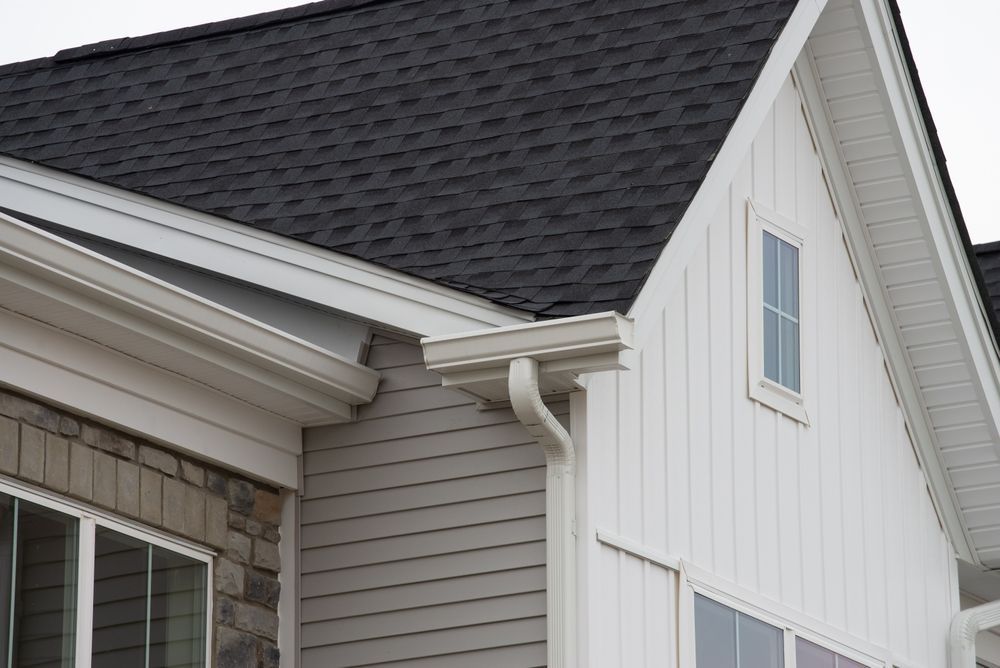 Corner of a house with a dark roof, white siding, and a gutter.