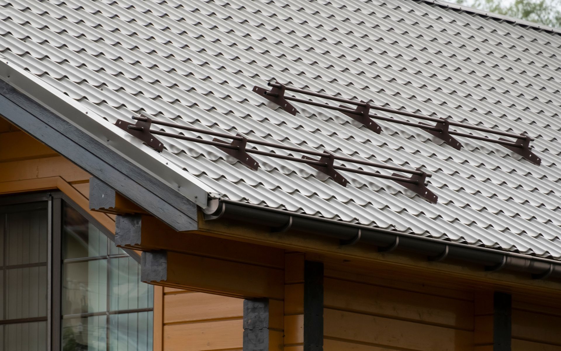 Metal roof with snow guards, over a wood-sided building. Brown gutter and trim are visible.