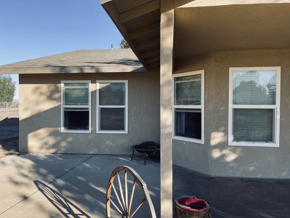 Beige building with white-framed windows, porch, and a wooden wheel in front on a sunny day.